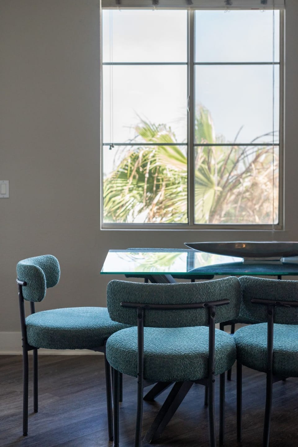 Dining area features a stylish glass-top table with six teal upholstered chairs.