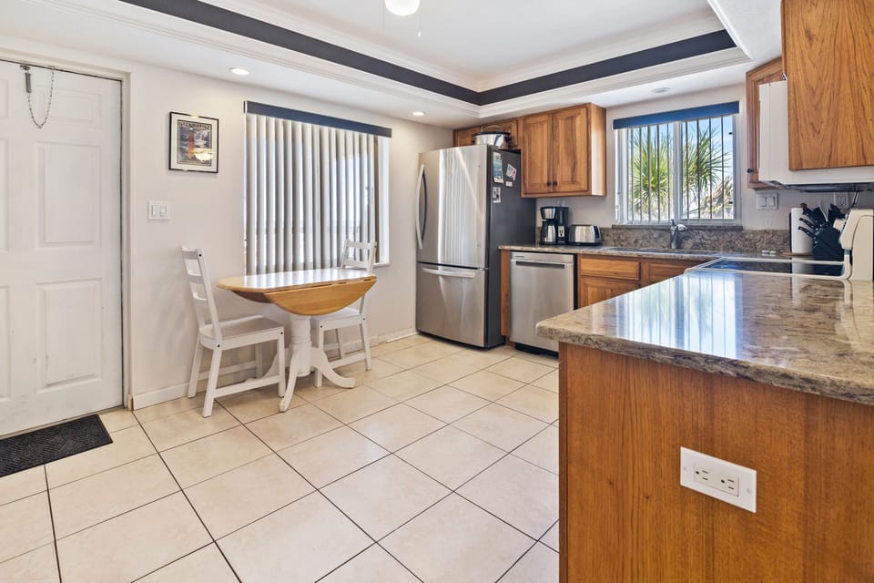 Enjoy a sunny start to your beach day in this fully equipped kitchen, featuring stainless steel appliances, granite counters, and a charming breakfast nook with coastal views.