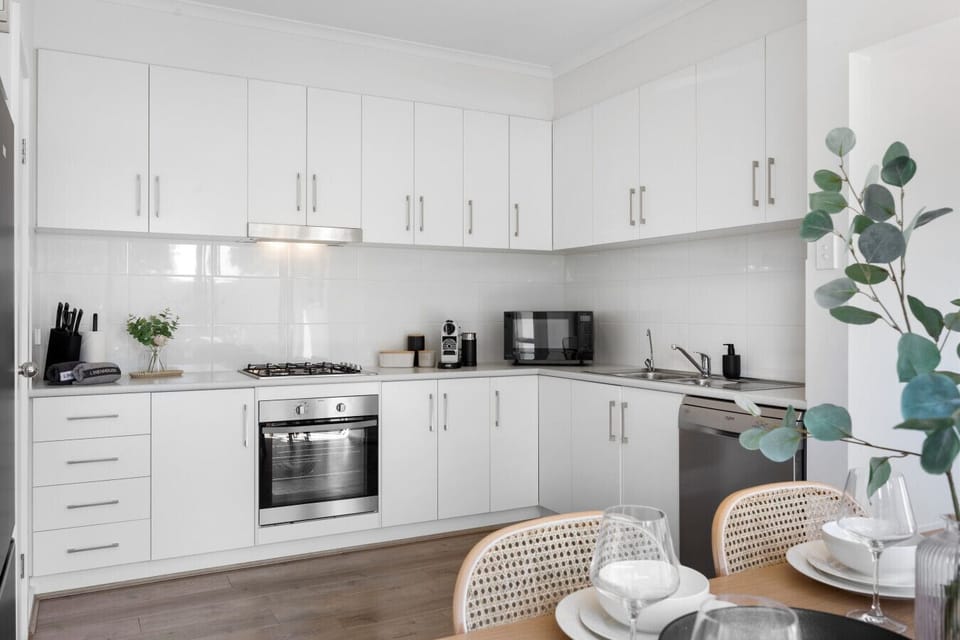 Cook with ease in the sleek white kitchen equipped with a gas stove, oven, fridge, microwave, dishwasher, coffee machine, and all essential cookware.