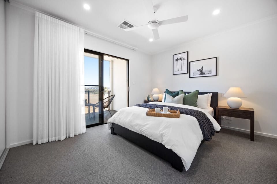 The primary suite offers a queen bed dressed in crisp linen, a built-in wardrobe, a ceiling fan, and a private balcony overlooking scenic farmland.