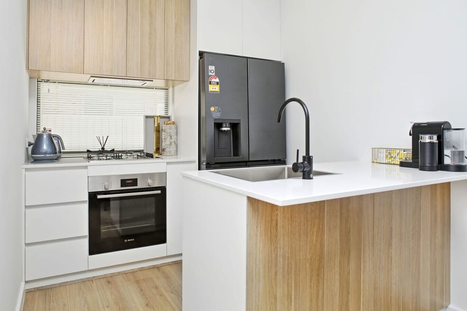 Light timber cabinets and a sleek black tap create a fresh backdrop for morning coffee and easy meal prep.
