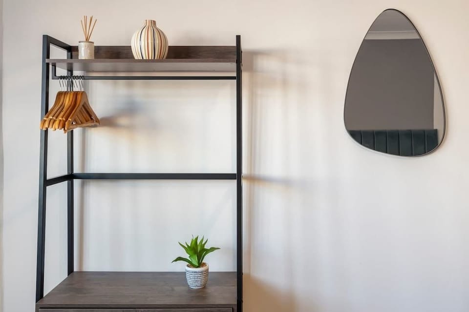 - Minimalist shelving unit with wooden hangers  
- Stylish wall mirror adds a modern clean finish  
- Touch of greenery brings warmth to the space  
