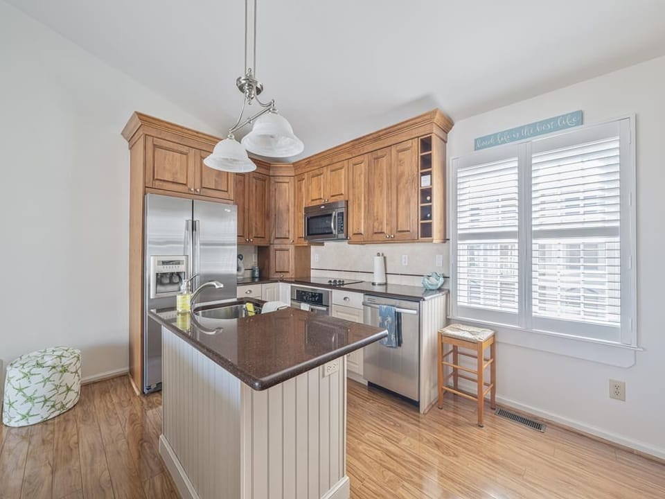 Sunny eat-in kitchen with island seating, wood cabinetry, and large windows.
