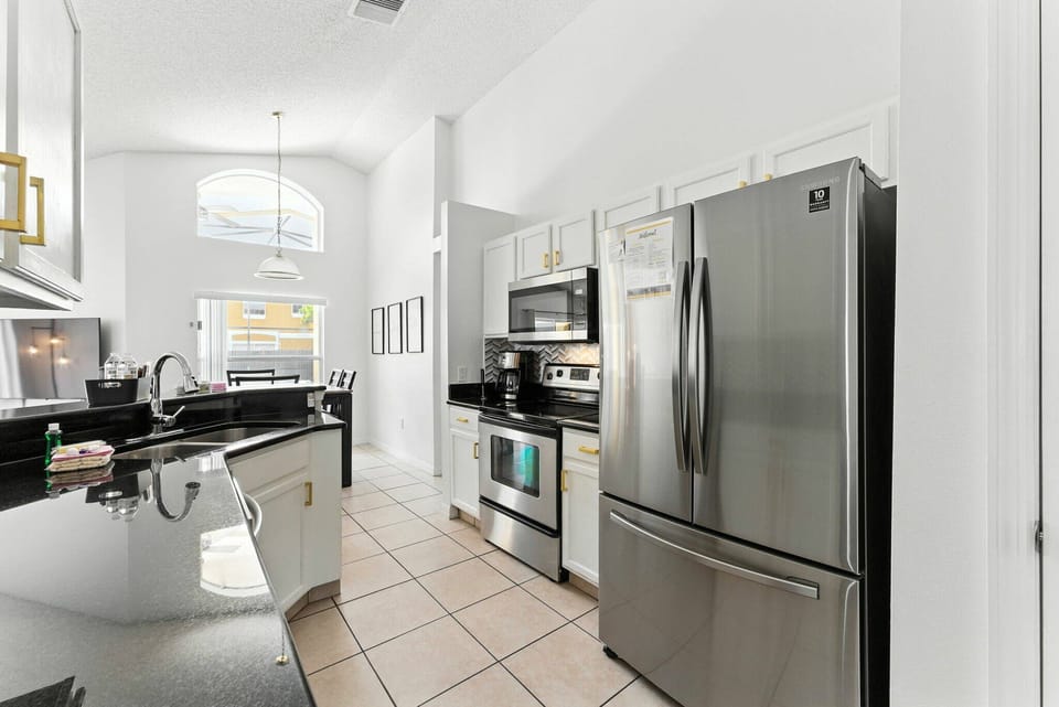Step into this sleek kitchen with polished black countertops and stainless steel appliances. The high ceilings and natural light create an airy space, ideal for culinary adventures or casual coffee chats with friends.
