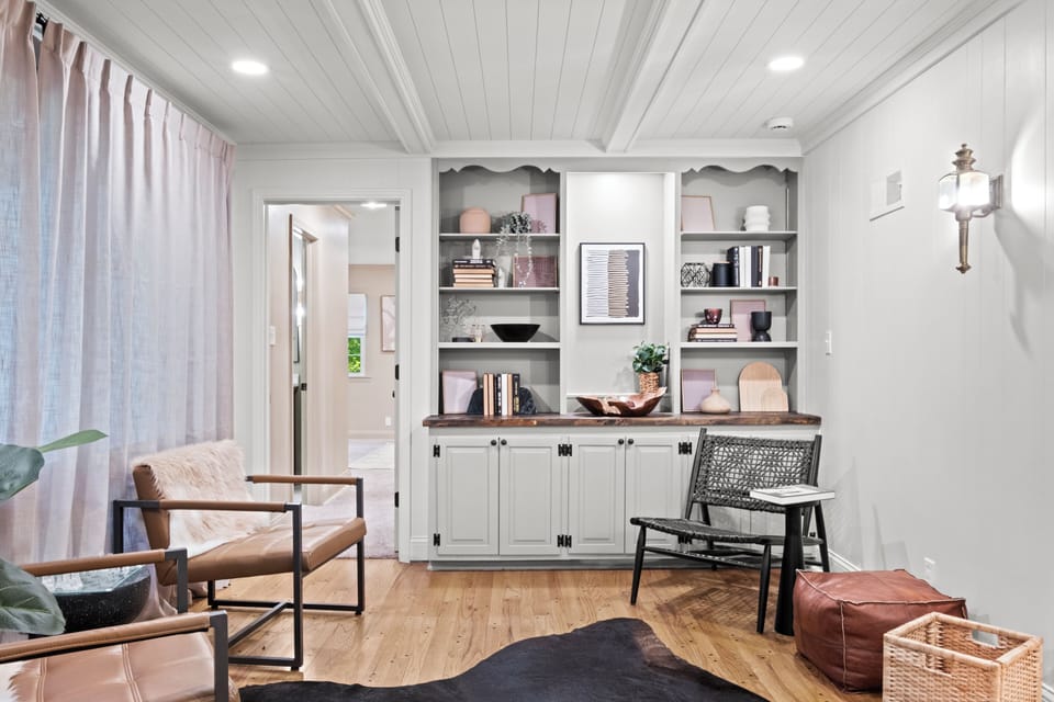 Cozy main-level sitting room featuring built-in shelving, comfortable chairs, and warm natural light. With patio access nearby, this is one of three separate living areas designed for comfort and connection.