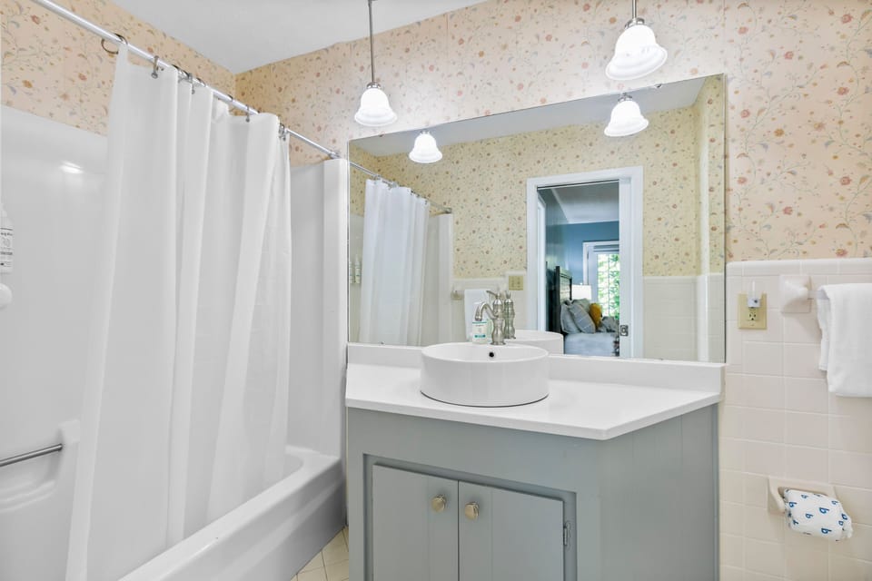 Bathroom with a corner vanity, vessel sink, floral wallpaper, and combination tub and shower.