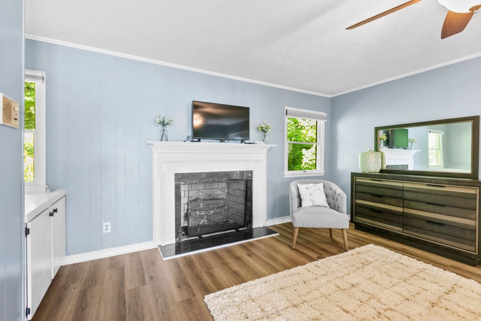 A room with light blue walls, a fireplace mantel with TV, and a wooden dresser.