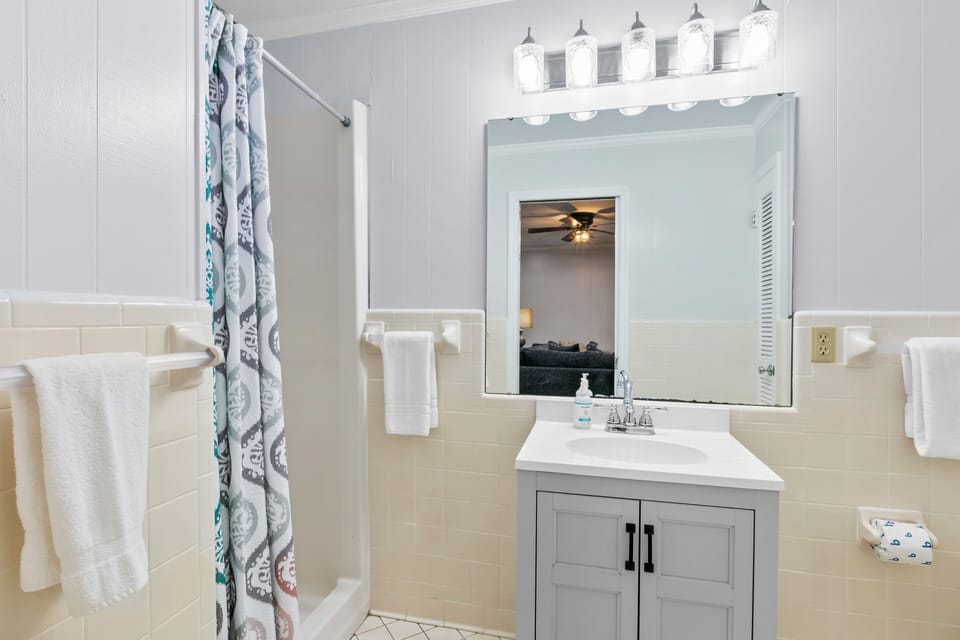 Bathroom featuring a grey single vanity, wall-width mirror, and walk-in shower.