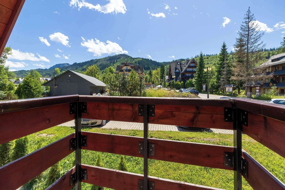  From the wooden balcony, there's a picturesque view of the Tatra Mountains and nearby houses.
