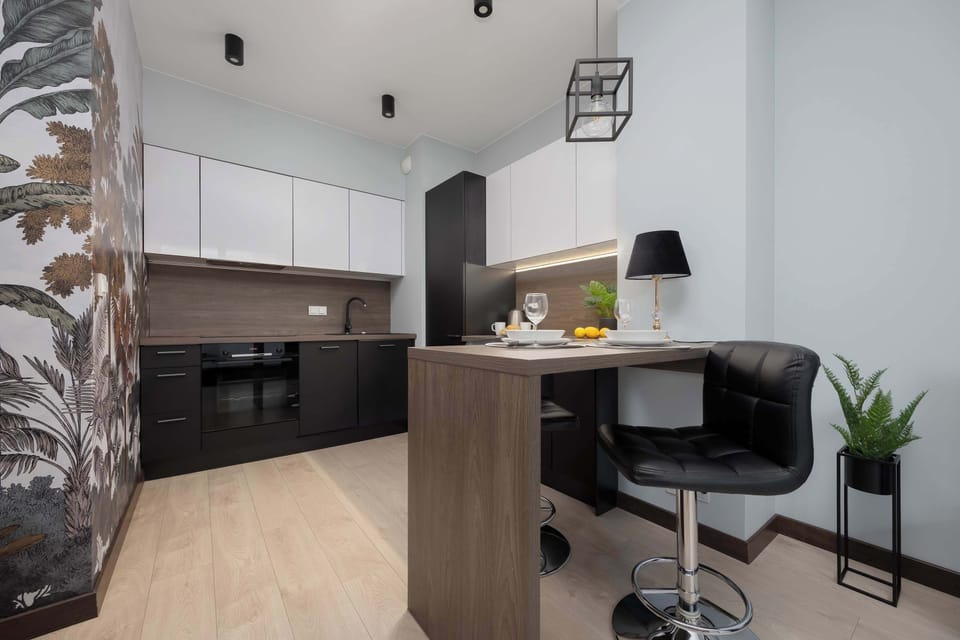 A modern kitchen featuring dark cabinetry and a light countertop with a small workspace and decorative plants. The design combines functionality with a sleek aesthetic.