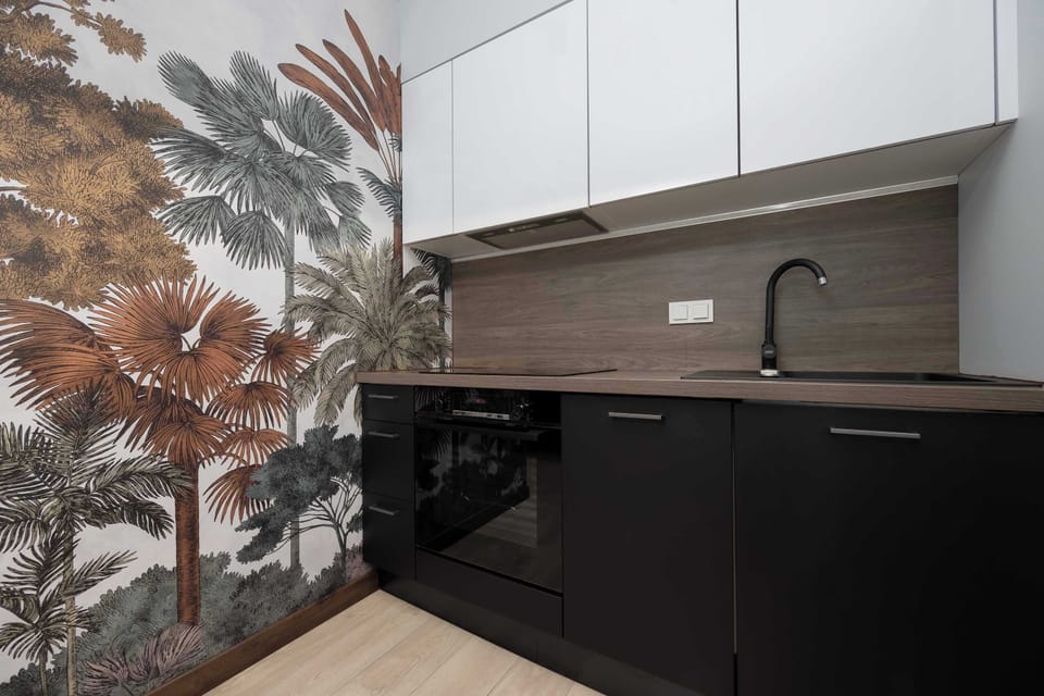 A modern kitchen with white upper cabinets and black lower cabinets, featuring a sink and stove with a stylish backsplash. The clean lines and neutral colors create a balanced look.
