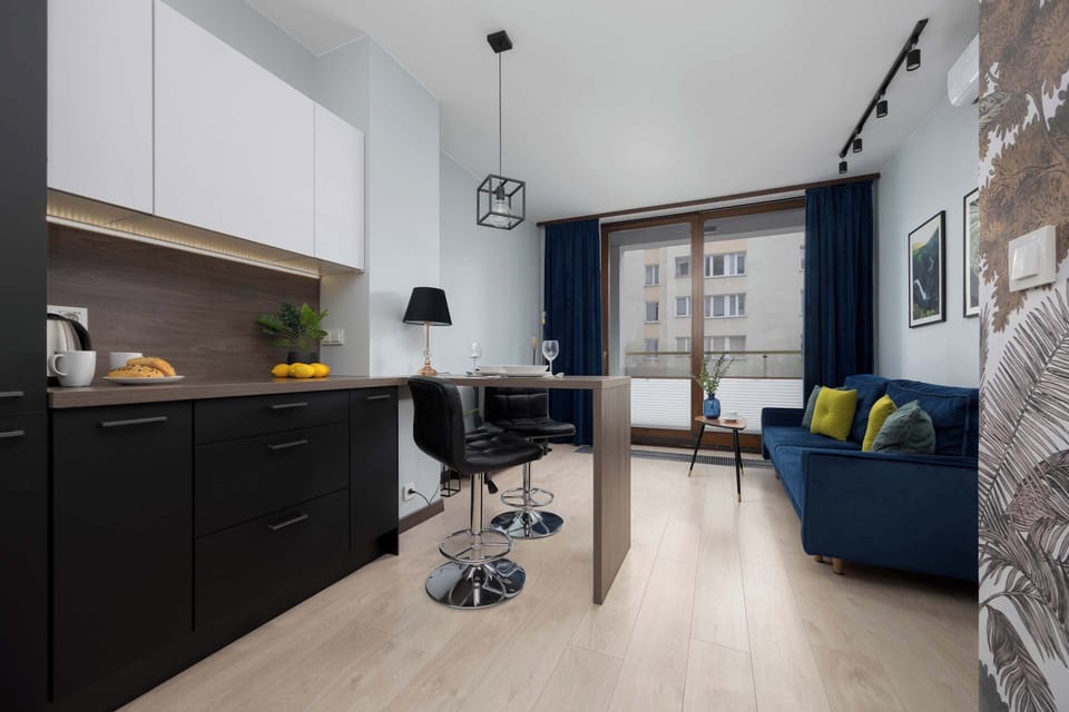 A view of the kitchen and living area, highlighting the open-plan layout and modern furnishings. The flooring is light wood, enhancing the room’s spaciousness.