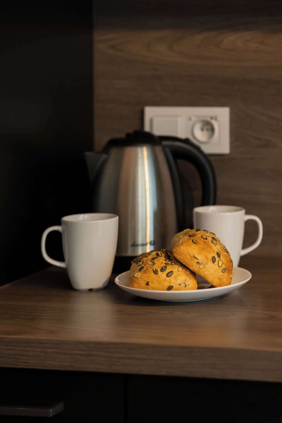 A close-up of a electric kettle with a cup and some breakfast items on a countertop, evoking a sense of comfort and daily routine. The dark cabinetry in the background adds depth to the scene