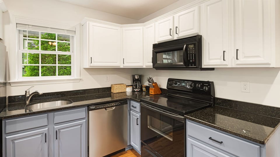 Every appliance you need is within reach — a black electric range, a stainless steel refrigerator, and dark granite counters that make prep feel easy.
