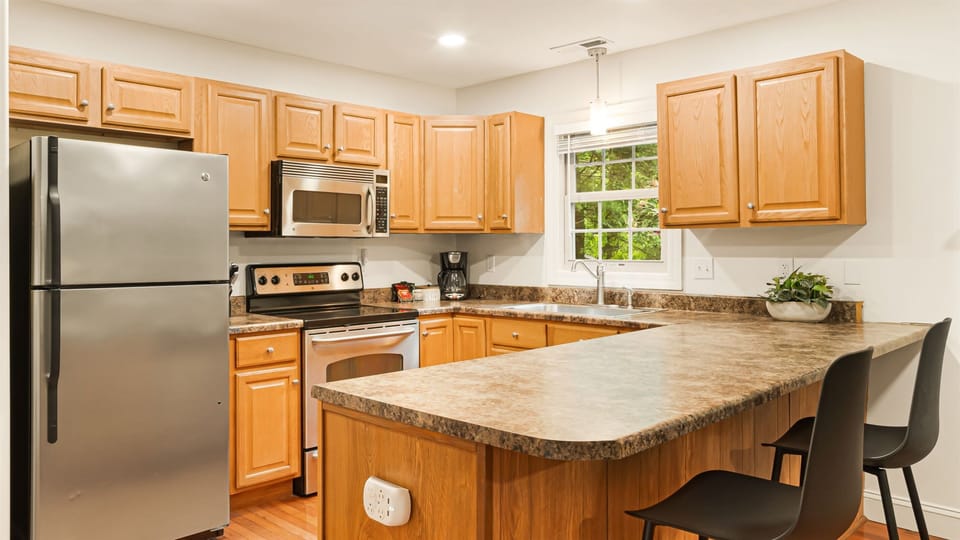 Laurel kitchen — full stainless steel appliances, bar seating at the peninsula counter, window overlooking the rhododendrons.