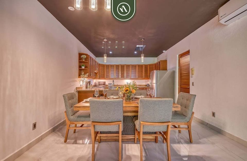Elegant wooden dining table surrounded by grey upholstered chairs, looking directly into the fully equipped kitchen.