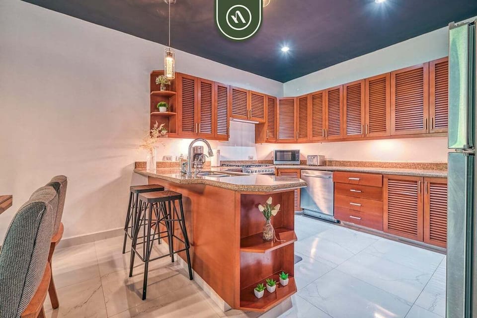 Spacious kitchen featuring rich wood cabinetry, granite countertops, stainless steel appliances, and a curved breakfast island with stools.