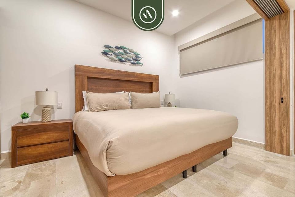 Wide view of a minimalist bedroom featuring a king bed with a rich wooden headboard and beige linens.