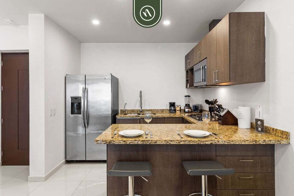 A well-designed kitchen space featuring dark wood cabinetry, beautiful granite countertops, a large stainless steel refrigerator, and a convenient breakfast bar with seating.