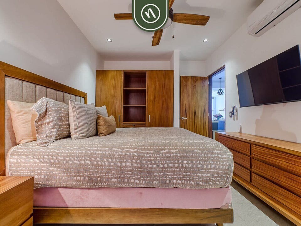 Spacious bedroom with a king bed, warm wood accents, and large windows bringing in natural light and balcony access.