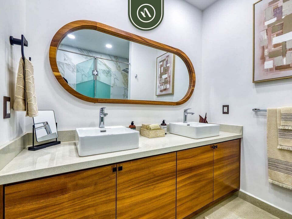 Stylish bathroom featuring a spacious wood vanity, two vessel sinks, contemporary fixtures, and a large statement mirror.