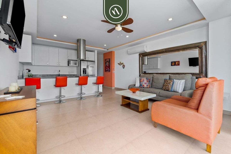 Relax in the spacious, air-conditioned living room with comfy seating and a large mirror. The space flows perfectly into the sleek, modern kitchen area.