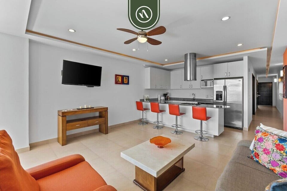 Relax in the spacious, air-conditioned living room with comfy seating and a large mirror. The space flows perfectly into the sleek, modern kitchen area.