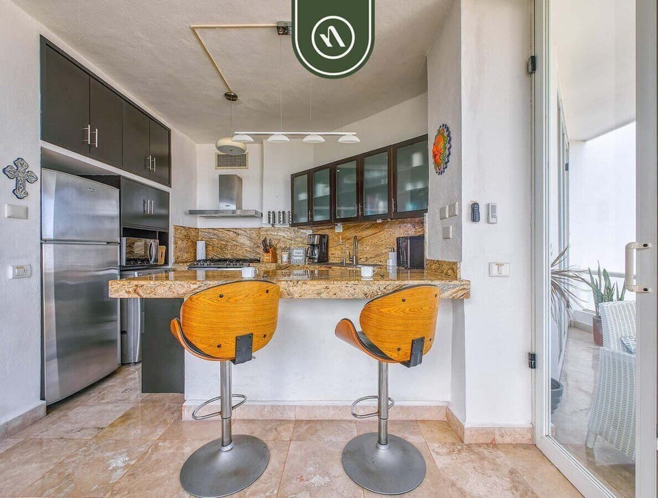 Close-up of the polished granite countertop featuring two stylish wooden bar stools, a stainless steel refrigerator, and modern cabinetry.