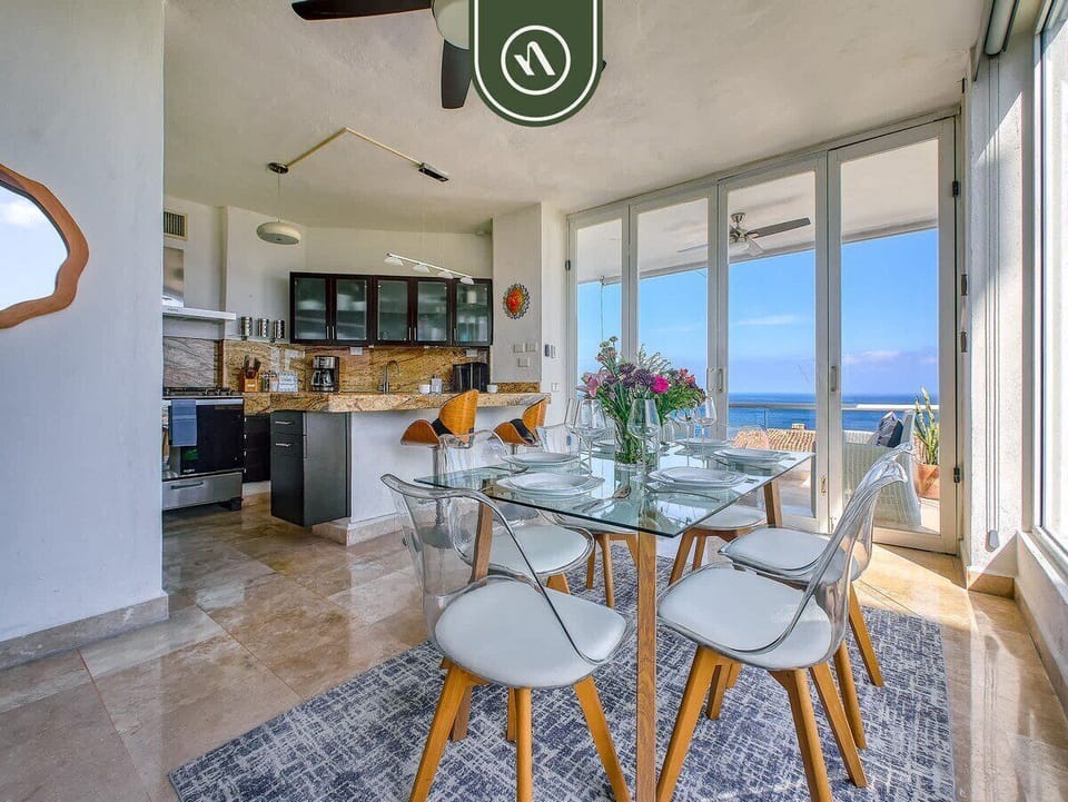 Wide perspective combining the elegant glass-top dining table and the fully equipped open kitchen with views of the ocean balcony.