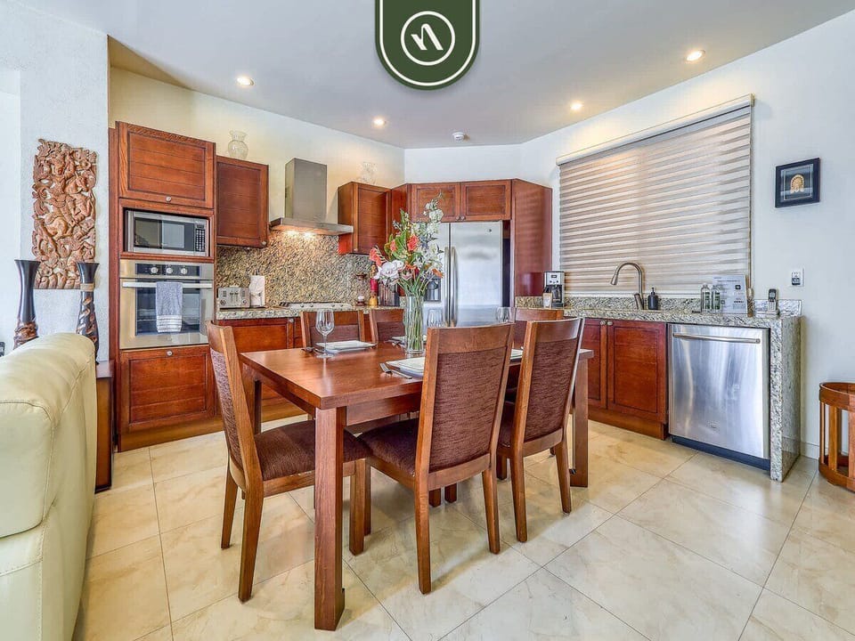 Gather around the solid wood dining table for a delicious meal. The open space leads directly into a fully-equipped kitchen with beautiful rich wood cabinetry and stone counters.