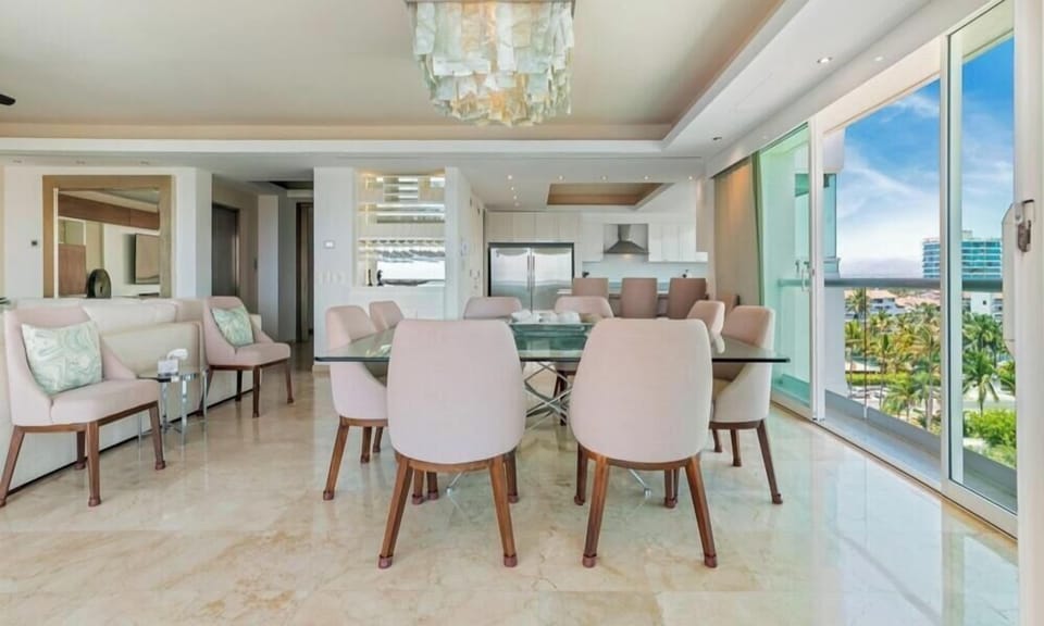 Sophisticated dining area featuring a glass table, pastel pink upholstered chairs, and a striking glass drop chandelier under a recessed ceiling.
