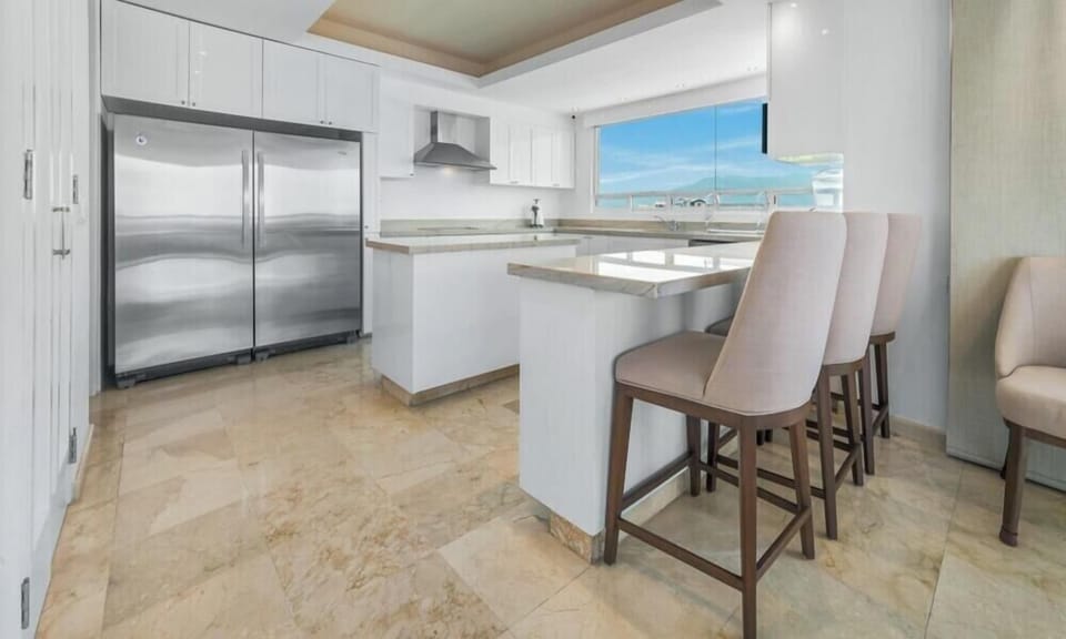 Clean kitchen space featuring white cabinetry, a large breakfast island with elegant high-back bar stools, and premium stainless steel appliances.