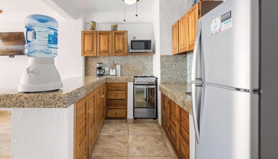 Classic kitchen layout featuring a stainless steel refrigerator, stove, wooden cabinetry, and a water dispenser.