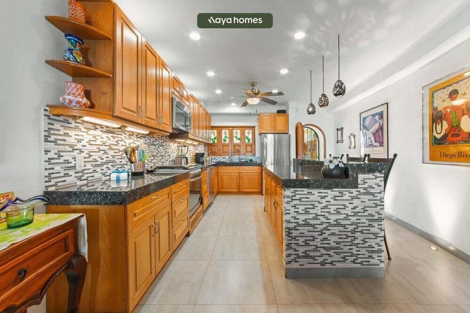 Well-lit kitchen hallway displaying dark polished granite countertops, warm wood cabinets, and overhead pendant lights.