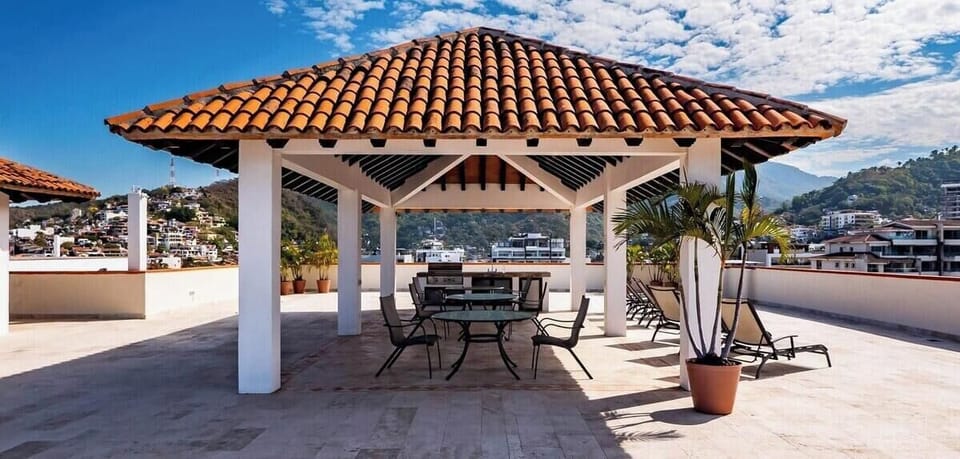 A large rooftop terrace under a traditional tiled pavilion roof, complete with outdoor dining setups and lounge chairs.