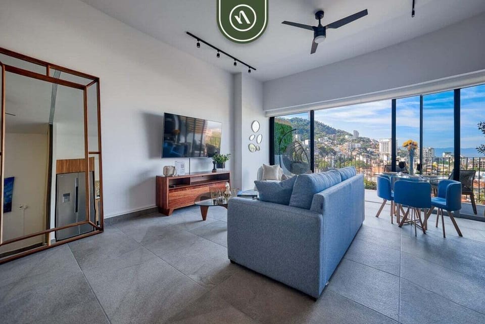 Bright, airy living room layout complete with a comfortable blue sofa, flat-screen TV, dining table, and large glass doors leading to the balcony.