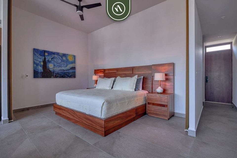 Comfortable king-size bed featuring a rich wood headboard, matching nightstands, and a vibrant painting on the wall.
