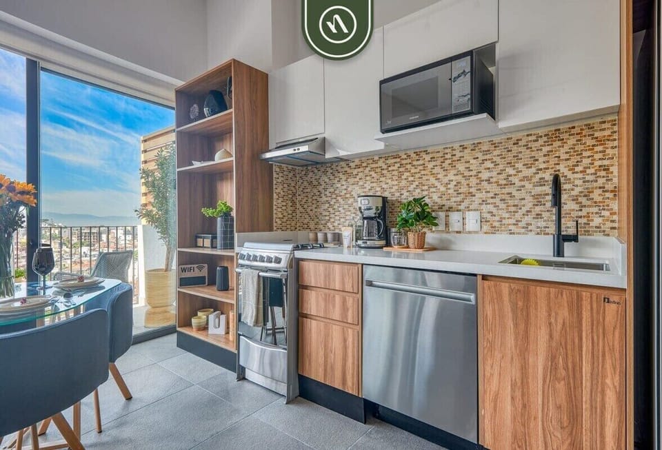 Contemporary kitchen featuring warm wood cabinetry, stainless steel appliances, a mosaic tile backsplash, and an adjacent balcony view.
