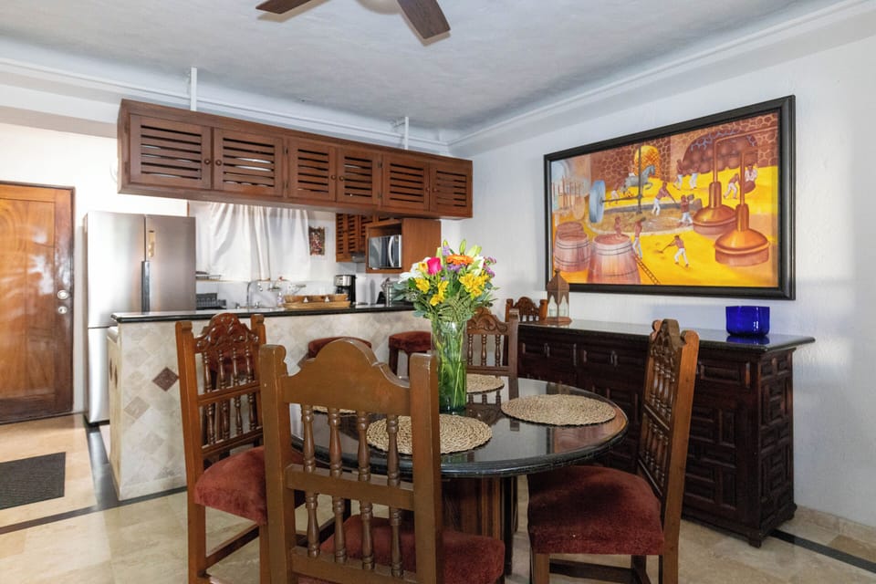 An open view of the dining area connecting to the kitchen, highlighting the breakfast bar, traditional wooden overhead cabinetry, and bright wall art.