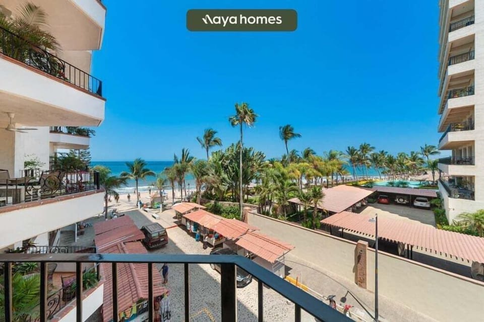 A scenic outdoor look from the private balcony terrace overlooking the sandy beach, ocean, and tropical palm trees.