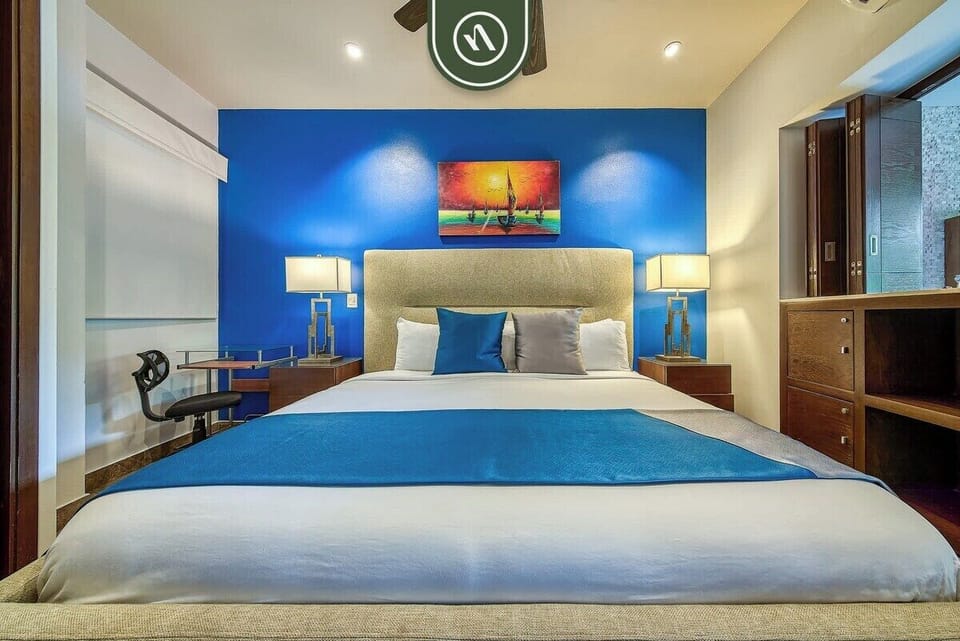 This bright, comfortable bedroom includes a dedicated desk area perfect for remote work, flanked by elegant lighting and vibrant tropical decor.