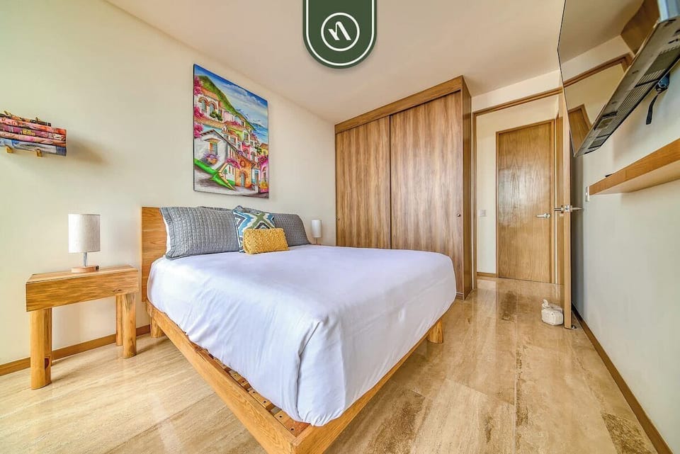 A broad view of the guest bedroom showing the warm wood flooring, matching bedside tables, a large built-in sliding wardrobe, and bright natural light.