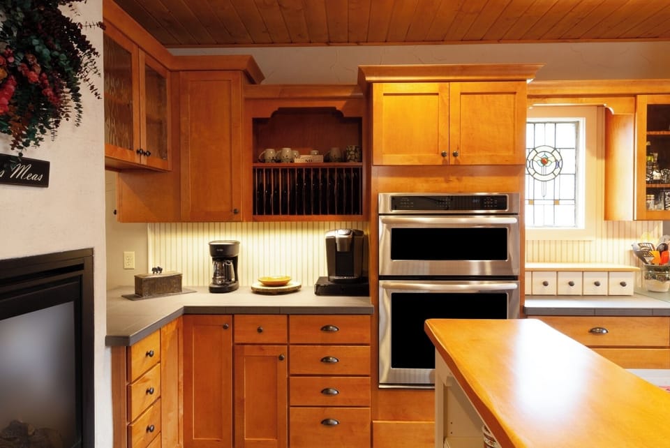 Your fully-equipped kitchen invites you to prepare meals with warm wood cabinets, modern appliances, and bright natural light streaming through stained glass.