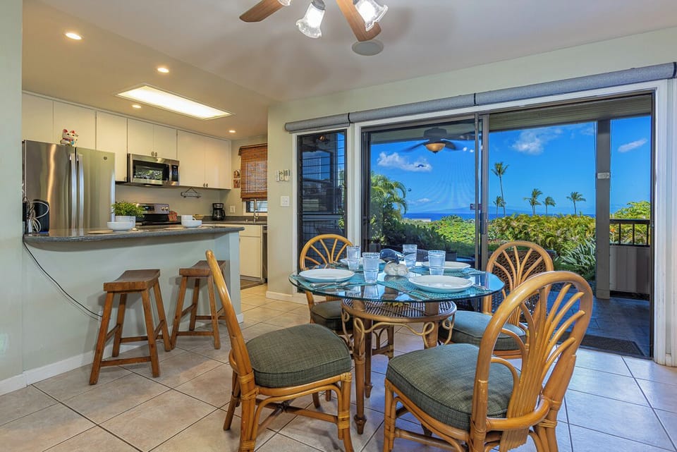 Step into your bright, island-style dining and kitchen area with stunning ocean vistas and tropical breezes. Enjoy meals at the glass-top table or relax at the breakfast bar, all while soaking in lush greenery and turquoise waters.