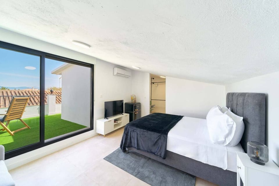 Double bed (135cm x 200cm), TV Stand with TV, fridge, and view of the terrace with outdoor furniture.