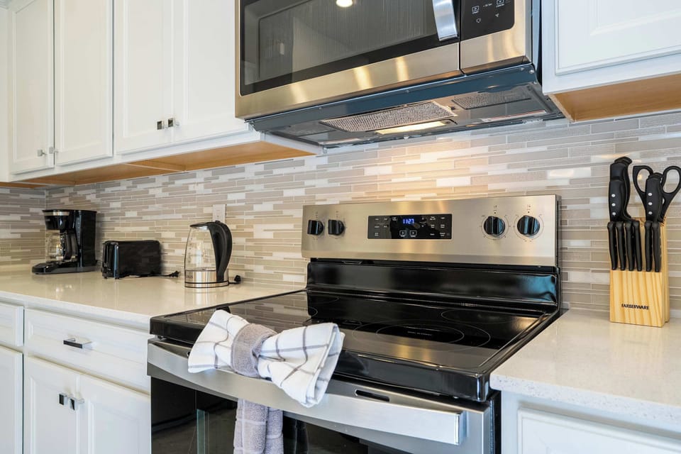 Prepare delicious meals with ease using the sleek stainless steel stove, modern backsplash, and a complete set of kitchen essentials.