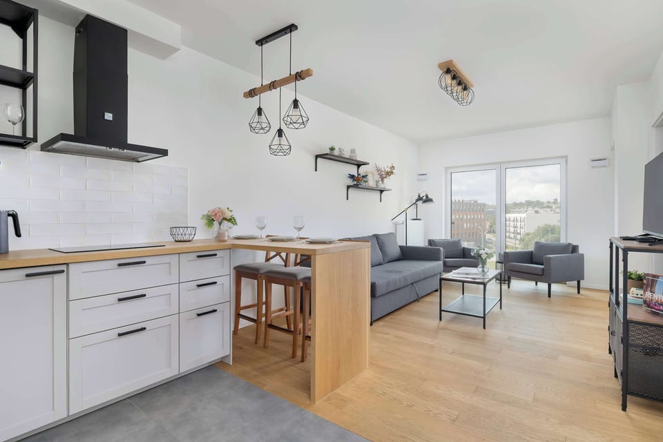 A stylish kitchen with black and white cabinetry and a small dining area. The modern pendant lights add a touch of sophistication.