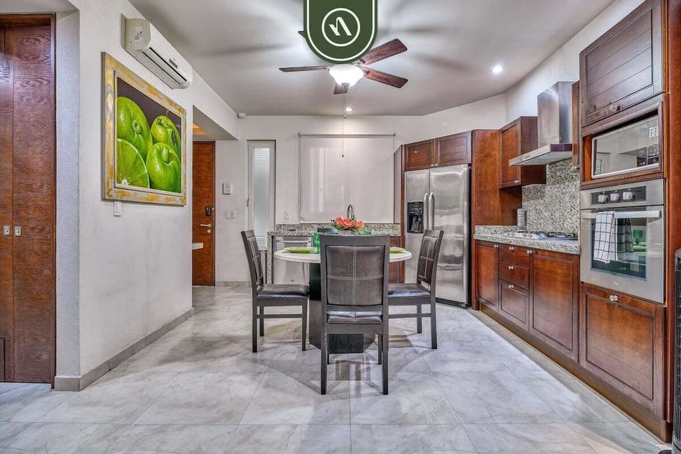 Prepare and enjoy meals in this open-concept space. It features a round dining table, vibrant artwork, and a fully equipped kitchen with rich wood cabinetry and stainless steel appliances.