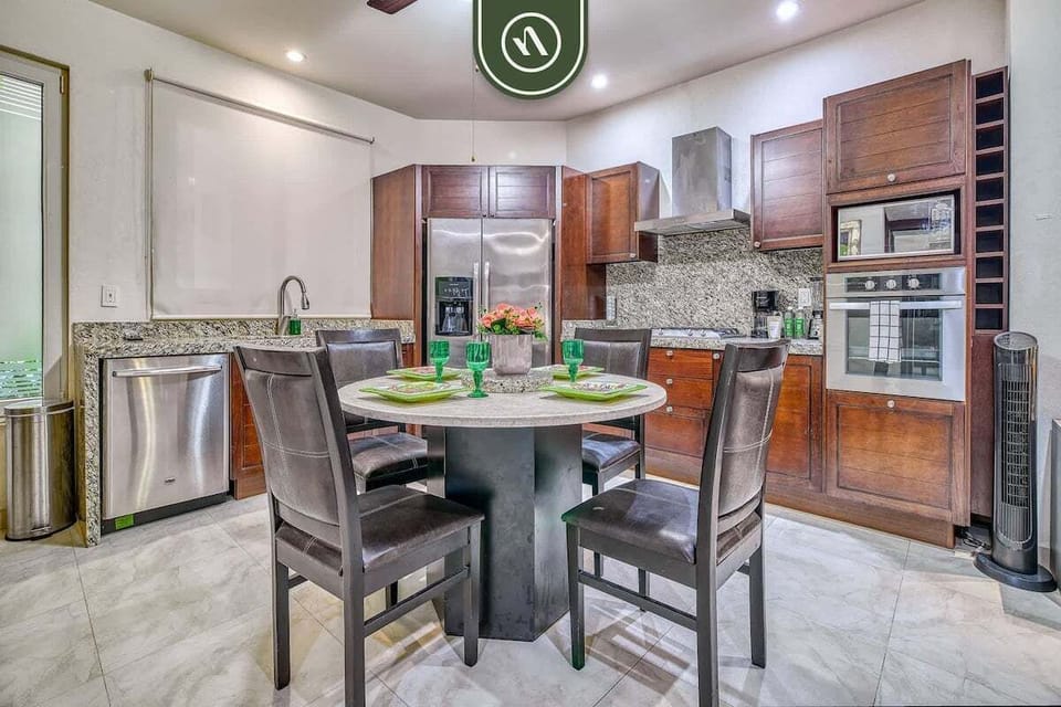 Enjoy home-cooked meals at the round dining table. The space opens to a fully equipped kitchen featuring rich wooden cabinetry, granite countertops, and modern stainless steel appliances.