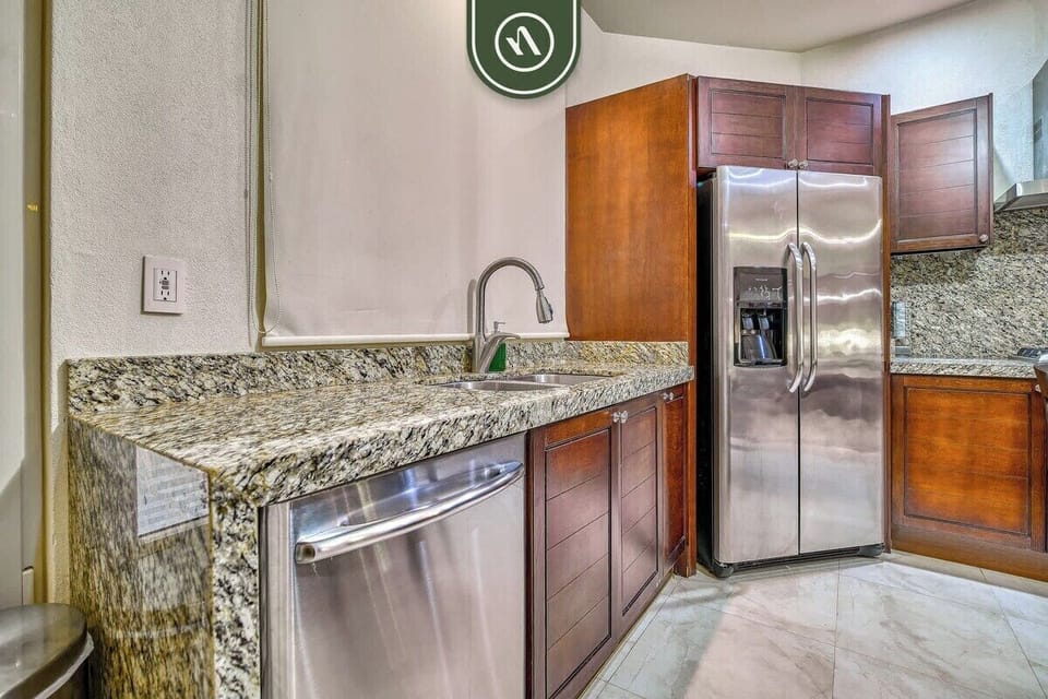 The kitchen is designed for your convenience, boasting high-quality stainless steel appliances including a dishwasher and a large double-door refrigerator alongside beautiful granite counters.